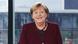 Angela Merkel, wearing a dark purple suit jacket, smiling at the camera