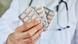 A white, male doctor's hand holding pill sleeves